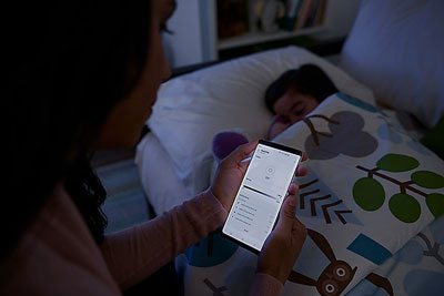  A woman controlling the light in the phone app, in front of a sleeping girl on a bed  